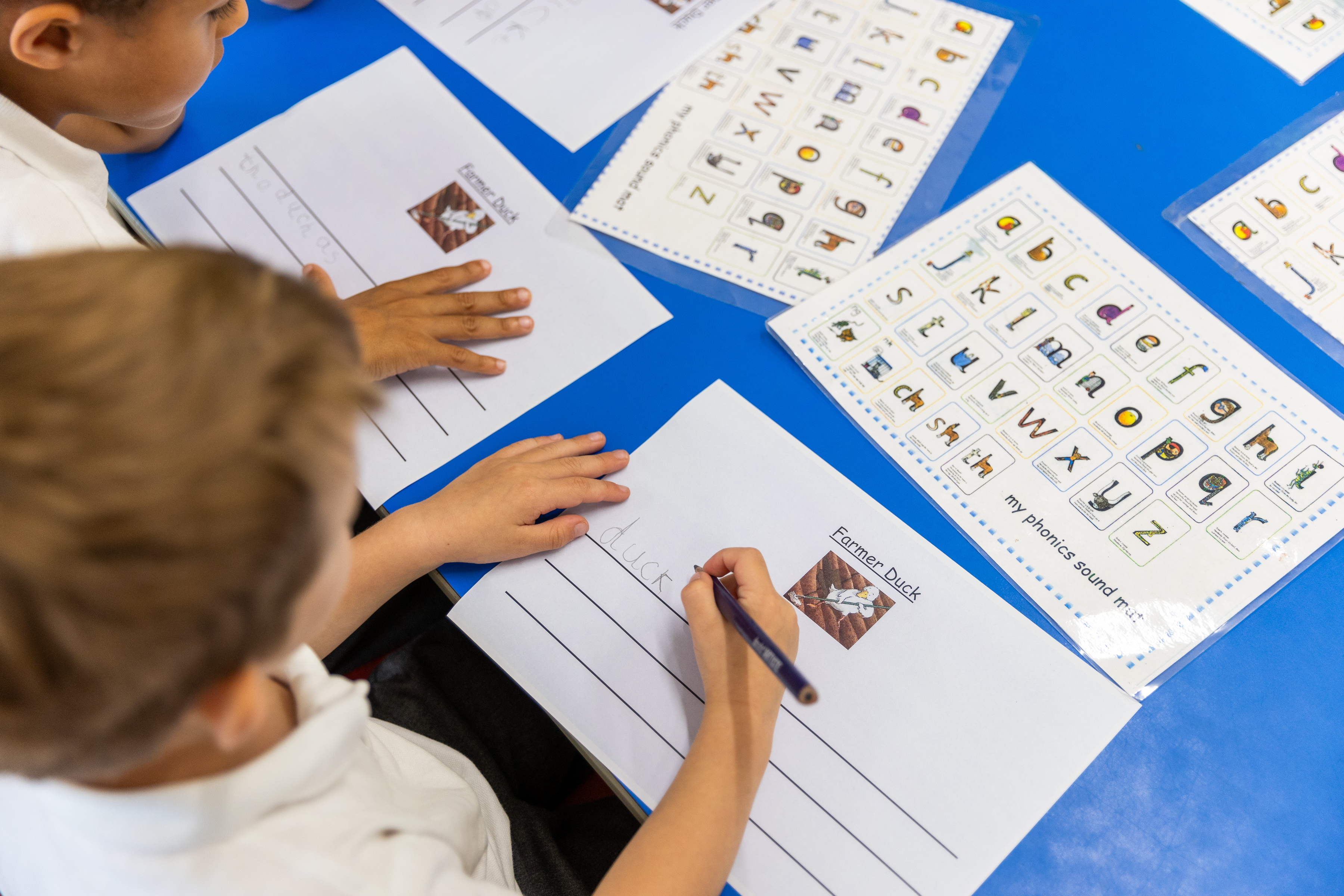 A teacher at Staplehurst School helping two students in early years with their work.